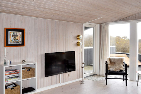 Wohnzimmer im Ferienhaus in Fanø mit Wand-TV, schwarzem Stuhl, Pelzdecke und Blick auf die Terrasse.