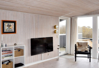 Woonkamer in vakantiehuis te Fanø met wand-tv, zwarte stoel met schapenvacht en zicht op het terras.