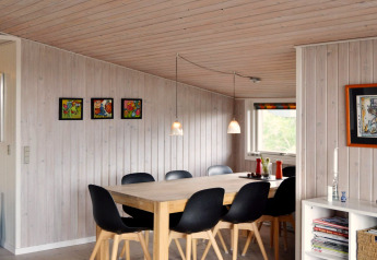 Coin repas dans une maison de vacances à Fanø, Danemark, avec chaises noires, table bois et œuvres colorées.