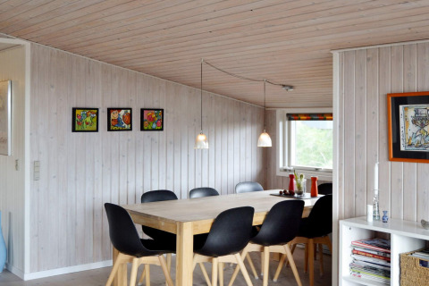Essbereich in einem Ferienhaus in Fanø, Dänemark, mit schwarzen Stühlen, Holztisch und Wandkunst.