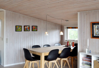 Eethoek in vakantiehuis in Fanø, Denemarken, met zwarte stoelen, houten tafel en kleurrijke wandkunst.