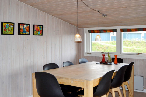 Sala da pranzo con tavolo in legno, sei sedie nere, quadri colorati e grandi finestre in un lodge a Fanø.