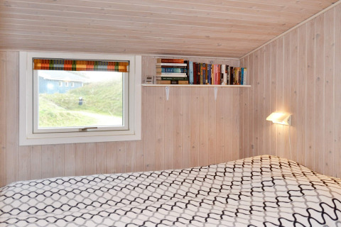 Schlafzimmer in einem Ferienhaus in Fanø, Dänemark, mit Holzvertäfelung, Bücherregal und Fensterblick.