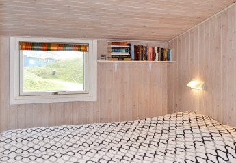 Slaapkamer in een vakantiehuis op Fanø, Denemarken, met houten wanden, boekenplank en raamuitzicht.