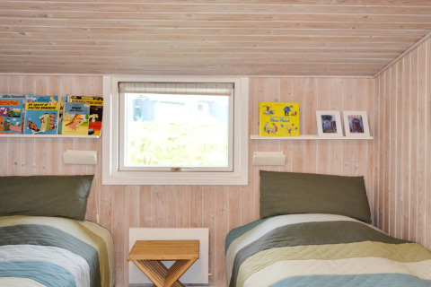 Camera in casa vacanza a Fanø, Danimarca: due letti singoli, libri e pareti in legno chiaro.