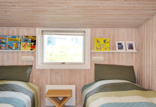 Schlafzimmer im Ferienhaus auf Fanø, Dänemark, mit zwei Einzelbetten, Büchern und Holzwänden.