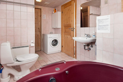 Bagno con lavatrice, WC, lavandino e vasca rossa in casa vacanze per 6 persone a Fanø, Danimarca.