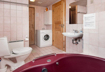 Baño con lavadora, inodoro, lavabo y bañera roja en casa vacacional para 6 personas en Fanø, Dinamarca.
