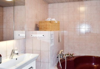 Badkamer met spiegel, wastafel, mand en bordeaux bad in een vakantiehuis op Fanø, Denemarken.