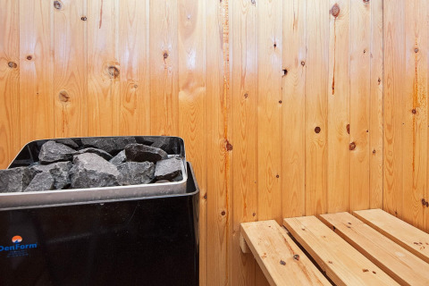 Vista interna di una sauna con pareti in legno, stufa e panca in una casa vacanze a Fanø, Danimarca.