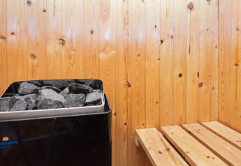 Vue intérieure d’un sauna avec murs en bois, poêle et banc dans une maison de vacances à Fanø, Danemark.