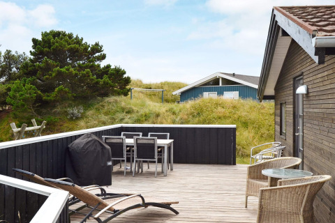 Terrasse eines 6-Personen-Ferienhauses in Fanø, Dänemark, mit Gartenmöbeln, Grill und Dünenblick.