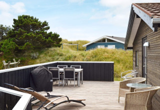 Terrasse eines 6-Personen-Ferienhauses in Fanø, Dänemark, mit Gartenmöbeln, Grill und Dünenblick.