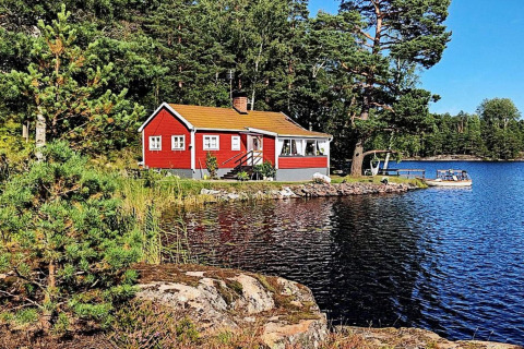 Red lodge by a peaceful lake surrounded by forest in ÅKERSBERGA, perfect for a relaxing getaway.