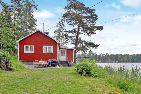 Red lakeside holiday home in Åkersberga, Sweden, surrounded by nature with garden seating and water view.