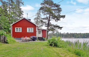 Rotes Ferienhaus am Seeufer in Åkersberga, Schweden, mit Garten und Blick auf den Wald und See.