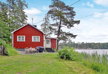 Rotes Ferienhaus am Seeufer in Åkersberga, Schweden, mit Garten und Blick auf den Wald und See.