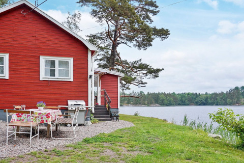 Red lakeside holiday home in Åkersberga, Sweden, with outdoor dining area and scenic water views.