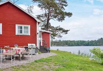 Rotes Ferienhaus am See bei Åkersberga, Schweden, mit Gartentisch, Grill und Blick auf den See.