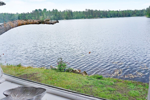 Vista di un lago tranquillo dalla finestra di una casa vacanza ad Åkersberga, Svezia, con alberi sullo sfondo.