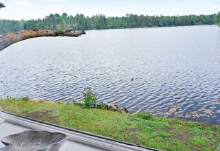 Vista di un lago tranquillo dalla finestra di una casa vacanza ad Åkersberga, Svezia, con alberi sullo sfondo.