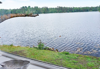 Blick auf einen See durch das Fenster eines Ferienhauses in Åkersberga, Schweden, mit Bäumen am Ufer.