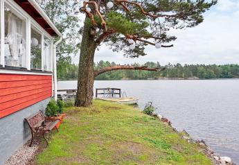Vue depuis un gîte à Åkersberga, Suède, avec façade rouge, banc, arbre et bateaux sur le lac.