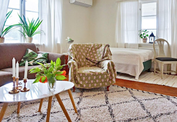 Wohnzimmer eines Ferienhauses in Åkersberga, Schweden, mit Sofa, Sessel, Pflanzen und Tageslicht.