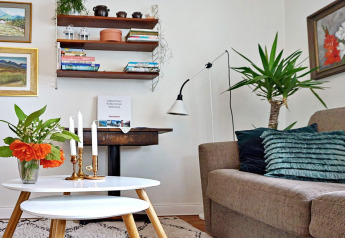 Wohnzimmer eines Ferienhauses in Åkersberga, Schweden, mit Sofa, Pflanzen, Kerzen und Wandregalen.