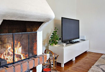 Wohnzimmer mit Kamin, Flachbildfernseher auf weißem TV-Schrank, Pflanze und Holzboden in Åkersberga, Schweden.
