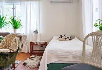Helles Schlafzimmer im Ferienhaus in Åkersberga, Schweden, mit Pflanzen, Sessel und Tageslicht.