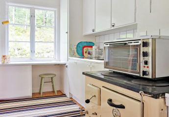 Helles Kücheninterieur mit Fenster, Ofen und Herd in einem Ferienhaus für 5 Personen in Åkersberga, Schweden.