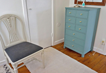 Helles Zimmer mit blauer Kommode, weißem Stuhl und Holzboden im Ferienhaus in Åkersberga, Schweden.