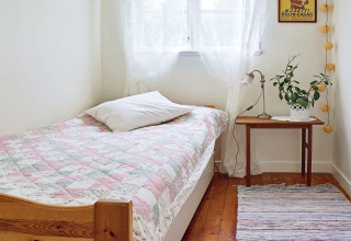 Helles und gemütliches Schlafzimmer mit Einzelbett, bunter Tagesdecke, Nachttisch und Fenster in Schweden.