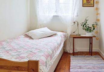 Helles und gemütliches Schlafzimmer mit Einzelbett, bunter Tagesdecke, Nachttisch und Fenster in Schweden.
