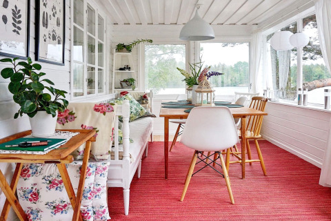 Bright holiday lodge in Åkersberga, Sweden, with floral cushions, red carpet, and lake view.