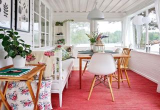 Bright holiday lodge in Åkersberga, Sweden, with floral cushions, red carpet, and lake view.