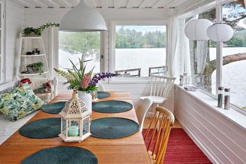 Bright dining area with lake view, wooden table, green cushions, and lantern at Åkersberga, Sweden lodge.