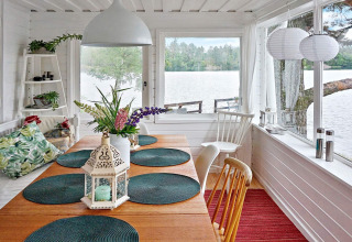 Helles Esszimmer mit Seeblick, Holztisch, grünen Kissen und Laterne im Ferienhaus in Åkersberga, Schweden.