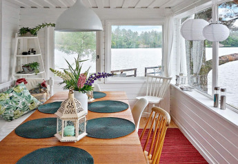 Helles Esszimmer mit Seeblick, Holztisch, grünen Kissen und Laterne im Ferienhaus in Åkersberga, Schweden.