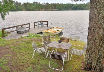Sitzbereich im Freien mit Tisch und Stühlen am See, Steg und gelbes Ruderboot, umgeben von Wald.