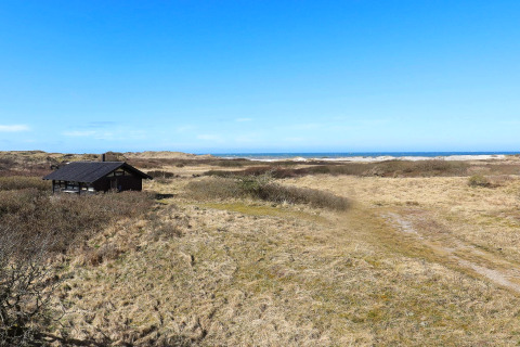 Udsigt til et sommerhus omgivet af klitlandskab med udsigt over havet, beliggende i Bindslev, Danmark.