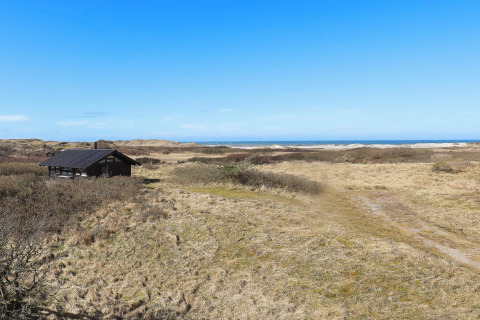 Ferienhaus im Dünengebiet mit Blick auf das Meer unter blauem Himmel in Bindslev, Dänemark.