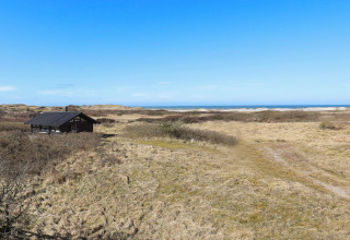 Udsigt til et sommerhus omgivet af klitlandskab med udsigt over havet, beliggende i Bindslev, Danmark.