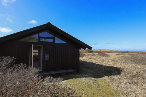 Schwarzes Chalet am offenen Feld unter blauem Himmel bei 4-Personen-Ferienhaus in Bindslev, Dänemark.