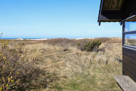 Udsigt fra en chalet i Bindslev, Danmark, med strandklitter, buske og blåt hav i det fjerne.