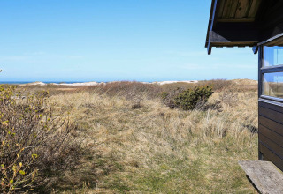 Vista da uno chalet a Bindslev, Danimarca, con dune sabbiose, erba, cespugli e mare sullo sfondo.