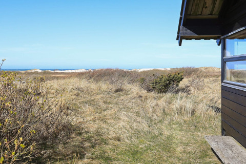 Udsigt fra en chalet i Bindslev, Danmark, med strandklitter, buske og blåt hav i det fjerne.