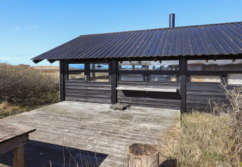 Outdoor deck and black wooden chalet at 4 person holiday home in Bindslev, Denmark, surrounded by nature.