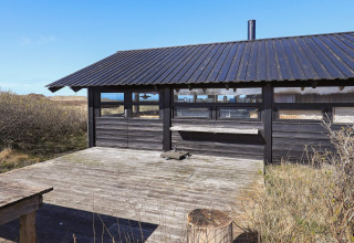 Udendørs terrasse og sort træchalet ved 4 personers feriehus i Bindslev, Danmark, med naturskøn udsigt.